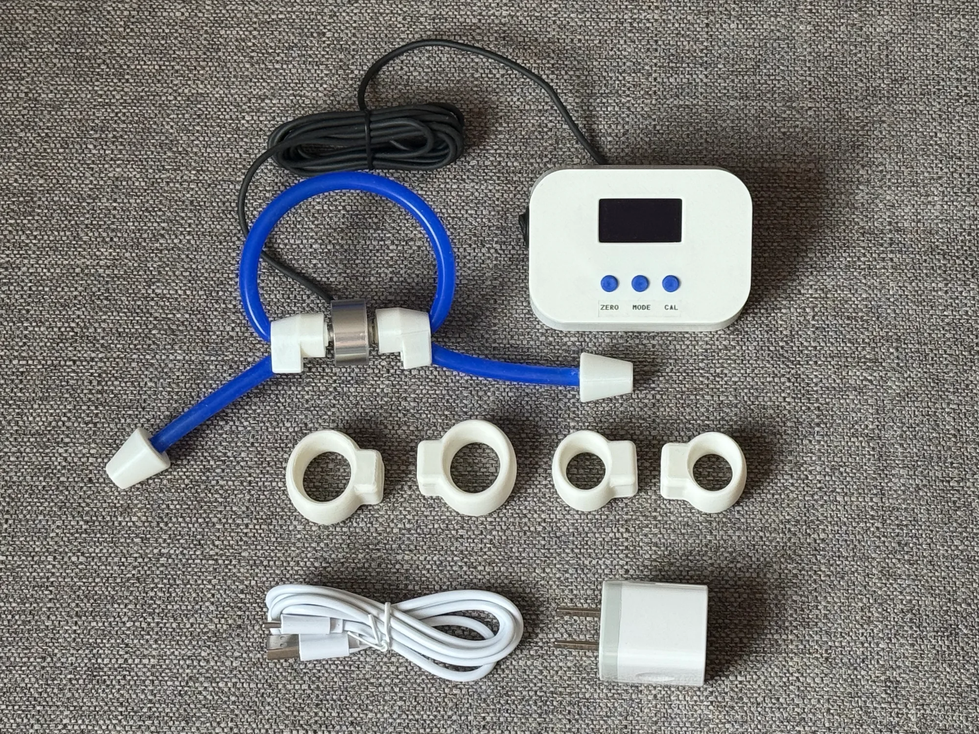 Splayometer Clinical Kit laid out — measurement unit, finger rings, hand loop, USB-C charger and cable